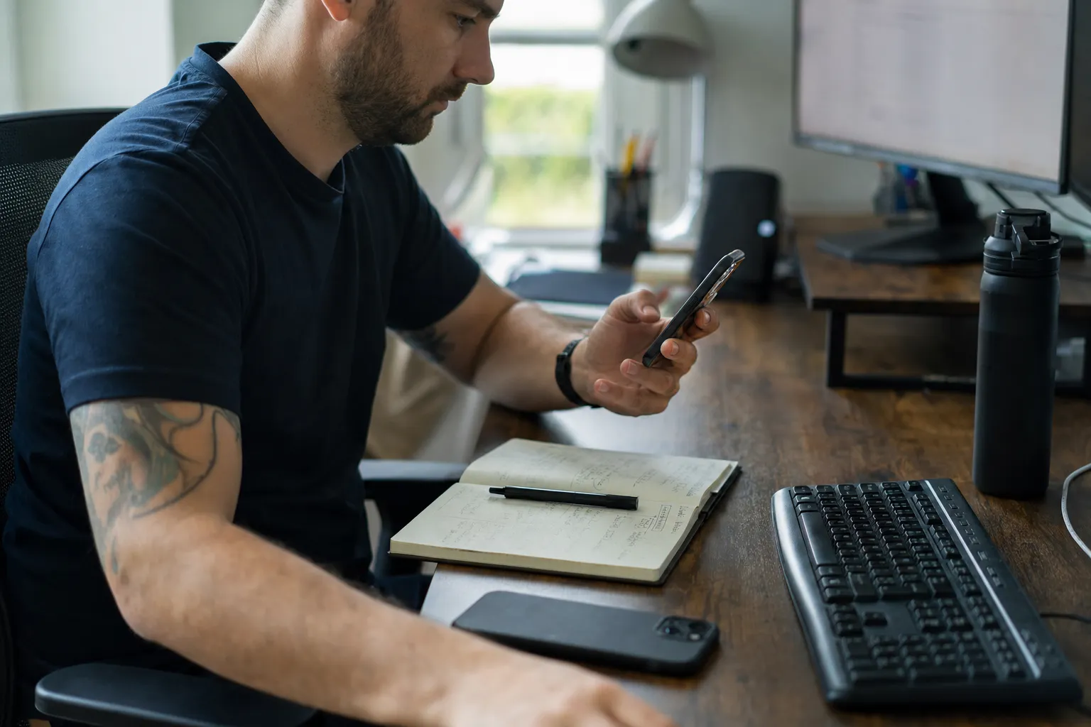 A trader at a home desk with two monitors, close on hands and notebook
